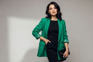 Stylowa kobieta w czarnej sukience i kolorowym żakiecie na neutralnym tle, naturalne oświetlenie.